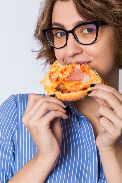 Junge Frau, welche die Pizza lokalisiert auf dem weißen Hintergrund schaut zur Kamera isst