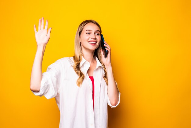 Junge Frau winkt mit den Händen, die durch das Smartphone über gelbe Wand sprechen