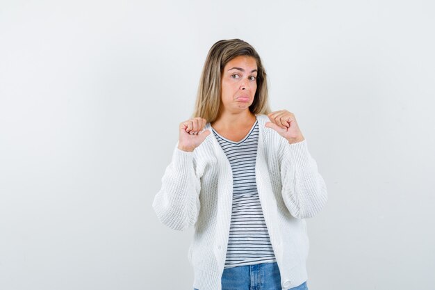 Junge Frau zeigt auf sich selbst mit Daumen in T-Shirt, Jacke und verwirrt, Vorderansicht.