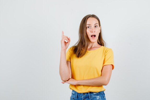 Junge Frau zeigt Finger in T-Shirt, Shorts und sieht überrascht aus