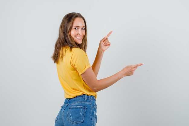 Junge Frau zeigt Finger weg und lächelt in T-Shirt, Shorts.