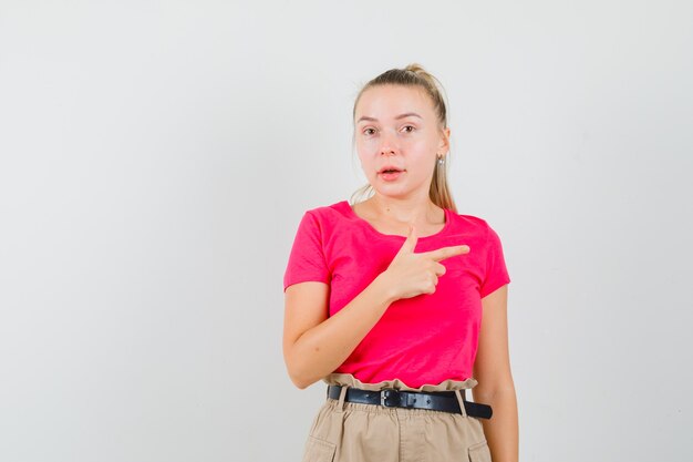 Junge Frau zeigt zur Seite in T-Shirts und Hosen und sieht erstaunt aus