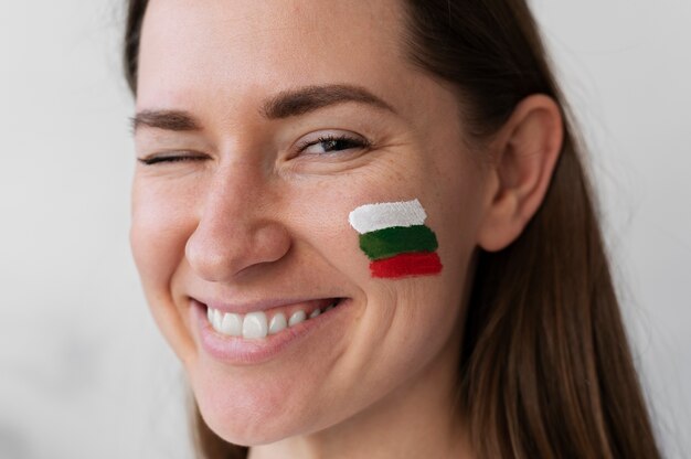 Junge Frau zwinkert mit bulgarischer Flagge auf die Wange gemalt