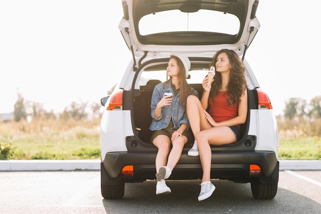 Junge Frauen, die auf Autokofferraum sitzen