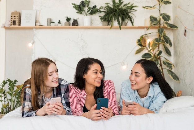 Junge Frauen, die auf Bett mit Smartphones liegen