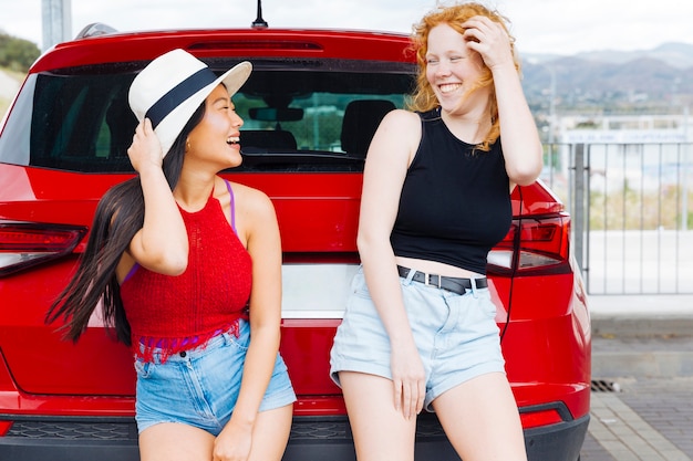 Junge Frauen, die rotes Auto und das Lachen bereitstehen