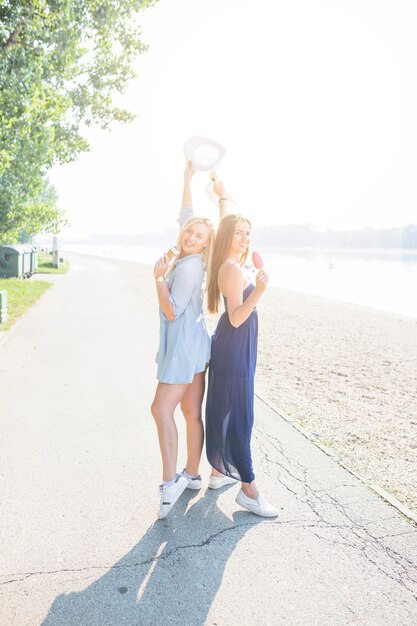 Junge Frauen, die zurück zu hinterem genießen Eiscreme am Strand stehen