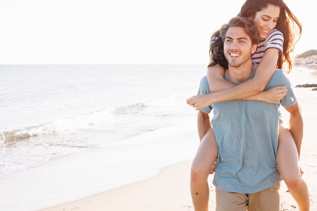 Junge Freund, der Freundin am Strand trägt