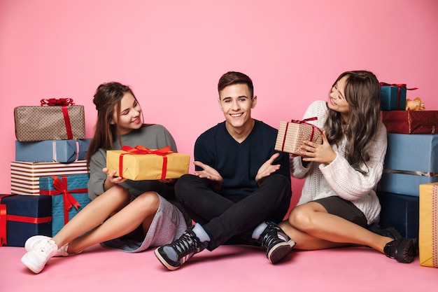 Junge Freunde sitzen unter Weihnachtsgeschenkboxen auf rosa