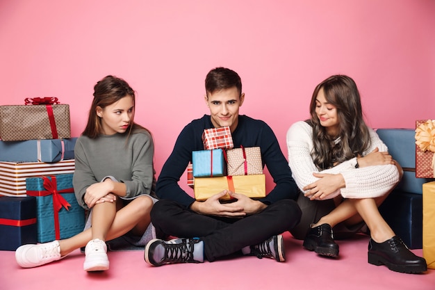 Junge Freunde sitzen unter Weihnachtsgeschenkboxen auf rosa