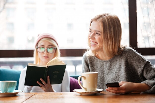 Junge Freundinnen, die Buch lesen und Kaffee trinken.