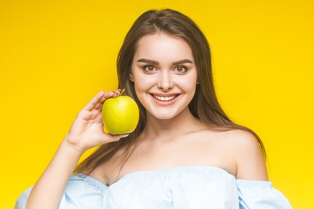 Junge fröhliche Frau mit Apfel, isoliert auf Gelb.