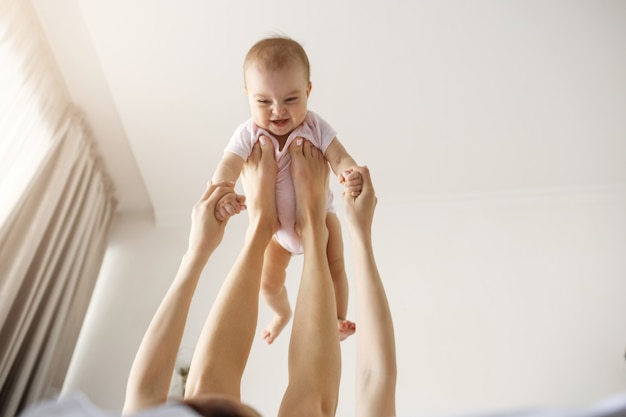 Junge fröhliche Mutter, die mit ihrem neugeborenen Baby spielt, das zu Hause auf dem Bett liegt.