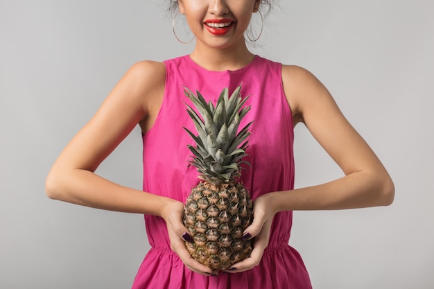 Junge gebräunte frau im rosa hemd, das ananas, positive emotion, isoliert, tropische frucht, diät, lächelnd, rote lippen hält