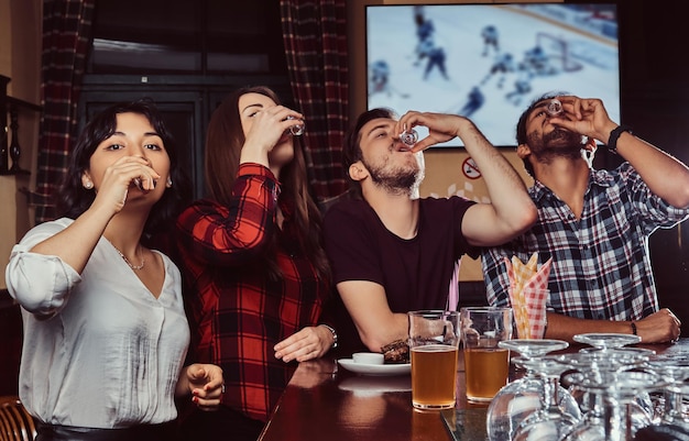 Junge gemischtrassige Freunde trinken Wodka und ruhen sich in der Kneipe aus.