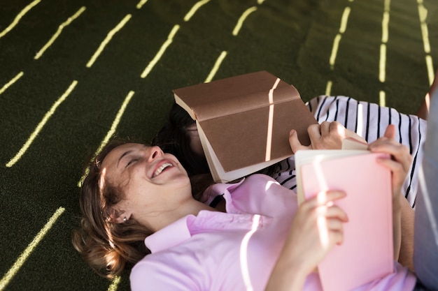 Kostenloses Foto junge gemischtrassige paare, die mit büchern auf schatten mit lichtscheinen liegen