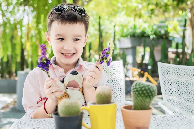 Junge genießen, mit Blume und Kaktus in einem Restaurant zu spielen - der Junge, der mit Naturkonzept glücklich ist