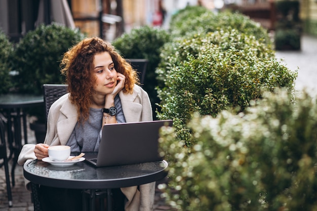 Junge Geschäftsfrau, die an einem Computer außerhalb des Cafés arbeitet