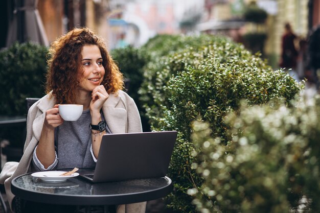 Junge Geschäftsfrau, die an einem Computer außerhalb des Cafés arbeitet