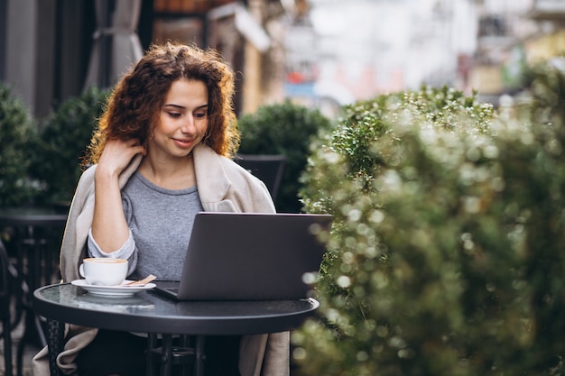 Junge Geschäftsfrau, die an einem Computer außerhalb des Cafés arbeitet