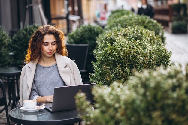 Junge geschäftsfrau, die an einem computer außerhalb des cafés arbeitet