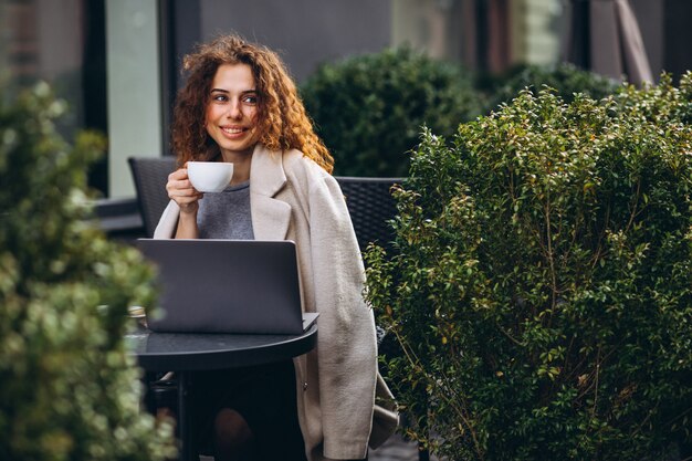 Junge Geschäftsfrau, die an einem Computer außerhalb des Cafés arbeitet