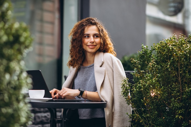 Junge Geschäftsfrau, die an einem Computer außerhalb des Cafés arbeitet