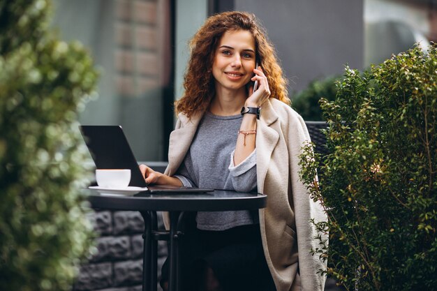 Junge Geschäftsfrau, die an einem Computer außerhalb des Cafés arbeitet