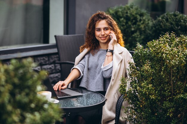 Junge Geschäftsfrau, die an einem Computer außerhalb des Cafés arbeitet