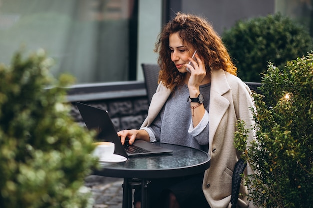 Junge Geschäftsfrau, die an einem Computer außerhalb des Cafés arbeitet