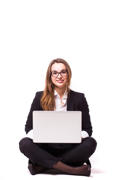 Junge Geschäftsfrau, die auf Boden sitzt und Laptop lokalisiert auf weißer Wand verwendet