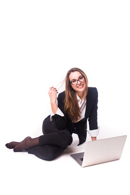 Junge Geschäftsfrau, die auf Boden sitzt und Laptop lokalisiert auf weißer Wand verwendet