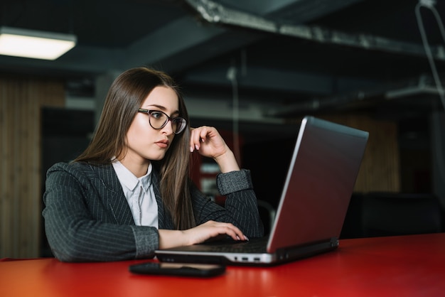 Junge Geschäftsfrau, die bei Tisch Laptop verwendet