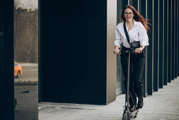 Junge Geschäftsfrau, die Elektroroller durch das Bürozentrum reitet