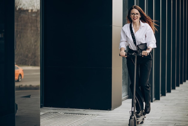 Junge Geschäftsfrau, die Elektroroller durch das Bürozentrum reitet