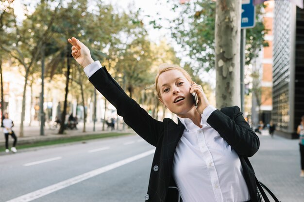 Junge Geschäftsfrau, die Hand für das Stoppen des Autos auf Stadtstraße anhebt