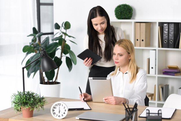 Junge Geschäftsfrau, die ihrem Kollegen im Büro etwas auf digitaler Tablette zeigt