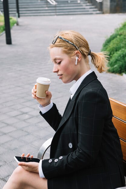 Junge Geschäftsfrau, die Kaffeetasse betrachtet Handy betrachtet