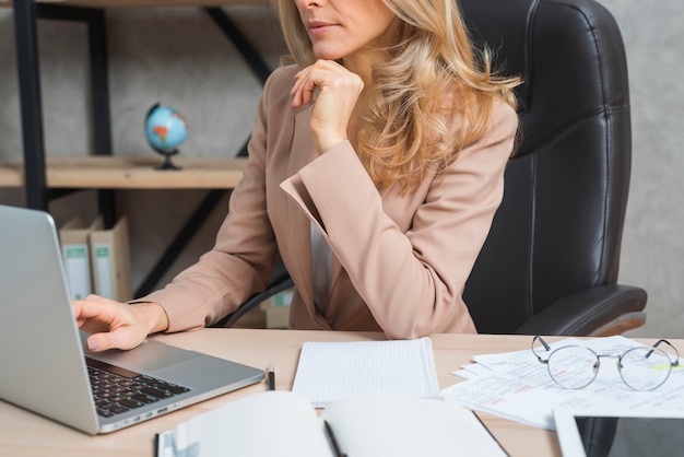 Junge Geschäftsfrau, die Laptop mit Tagebuch und Dokumenten am Arbeitsplatz verwendet