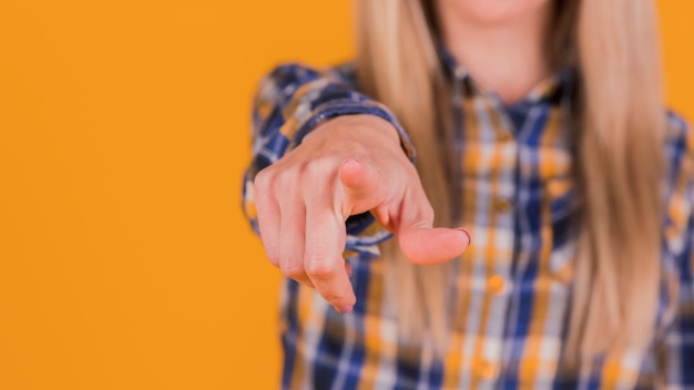 Junge Geschäftsfrau, die seinen Finger in Richtung zur Kamera gegen orange Hintergrund zeigt