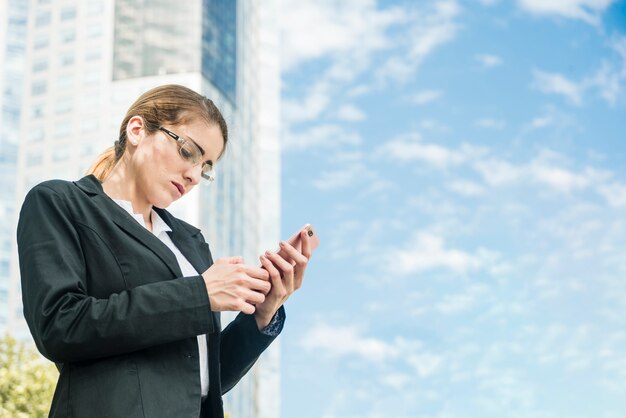 Junge Geschäftsfrau, die vor simsender Mitteilung des Gebäudes am Handy steht