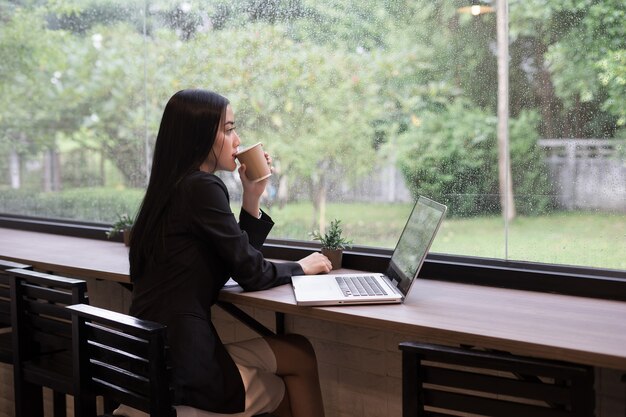 Junge Geschäftsfrau haben eine Pause mit Kaffee beim Arbeiten an Laptop im Büro