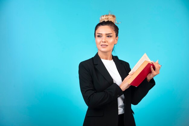 Junge Geschäftsfrau im schwarzen Blazer, der ein Aufgabenbuch hält und es liest.