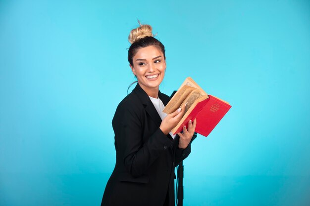 Junge Geschäftsfrau im schwarzen Blazer hält ein Aufgabenbuch und fühlt sich positiv.