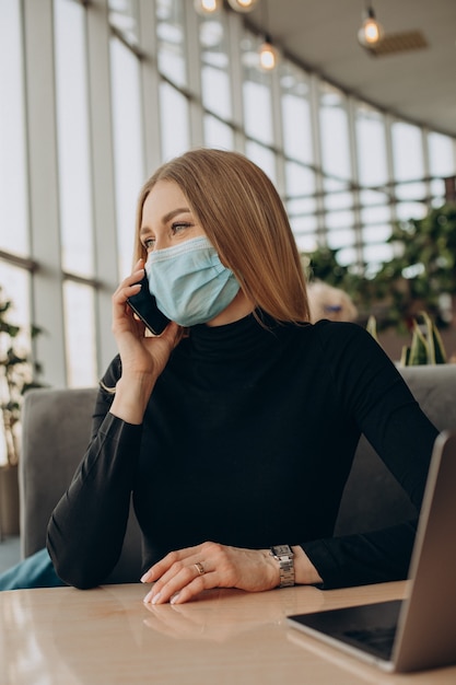 Junge Geschäftsfrau in der Maske, die an Laptop in einem Café arbeitet