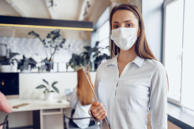 Junge Geschäftsfrau mit Gesichtsmaske, die im Büro steht und die Zwischenablage mit Dokumenten hält