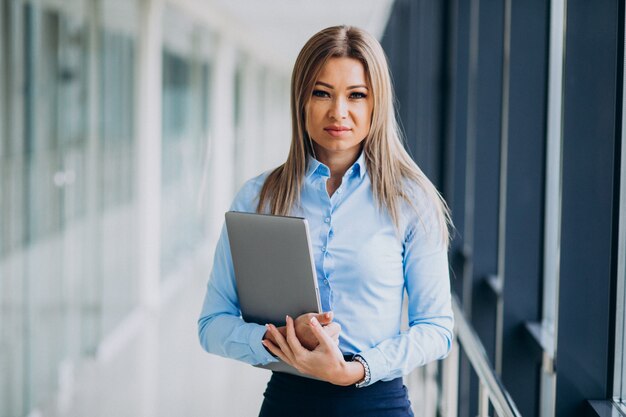 Junge Geschäftsfrau mit Laptop, der in einem Büro steht