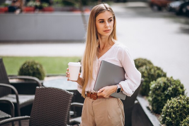 Junge Geschäftsfrau mit trinkendem Kaffee des Laptops außerhalb des Cafés