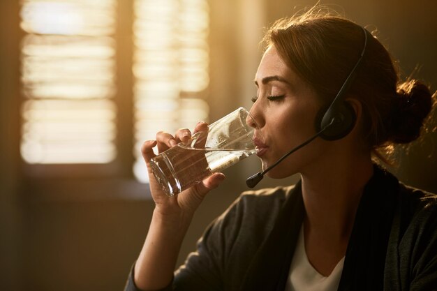 Junge Geschäftsfrau trinkt Wasser mit geschlossenen Augen, während sie eine Pause im Büro macht