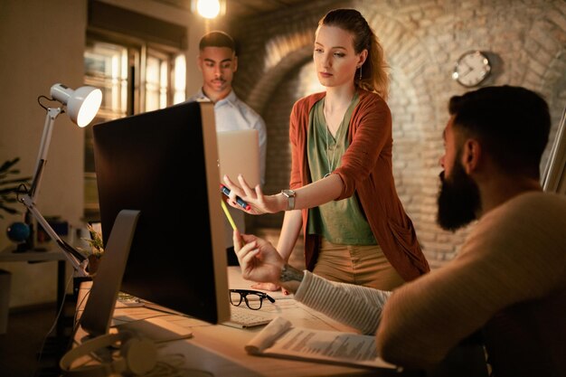 Junge Geschäftsfrau und ihre Kollegen beim Brainstorming, während sie einen Desktop-PC im Büro verwenden